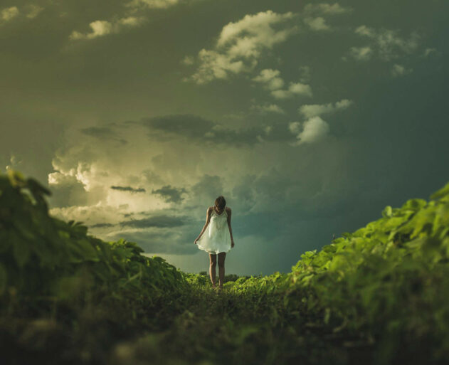 woman wearing white dress standing on hill with green grass under white cloudy sky